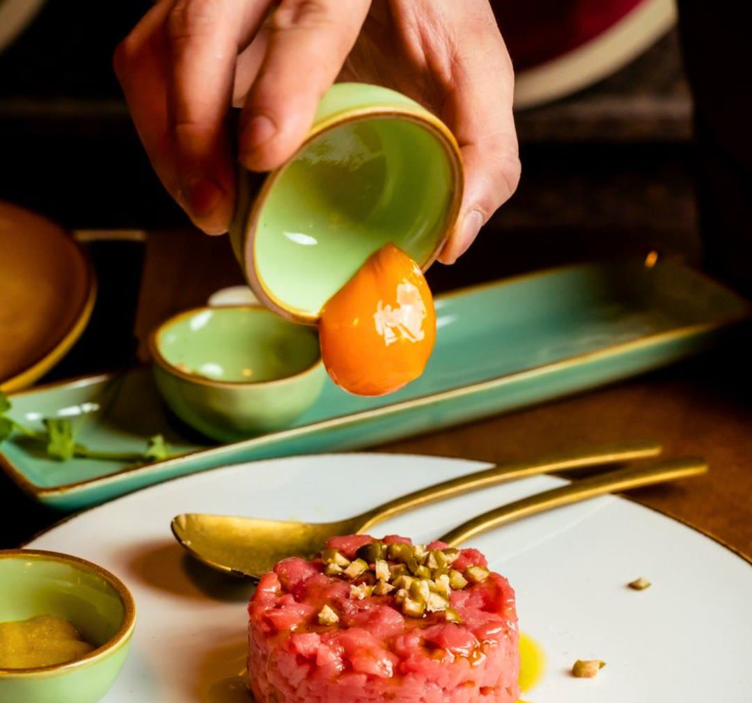 Tartare battuta al coltello con granella di pistacchio, mentre il tuorlo viene versato sopra